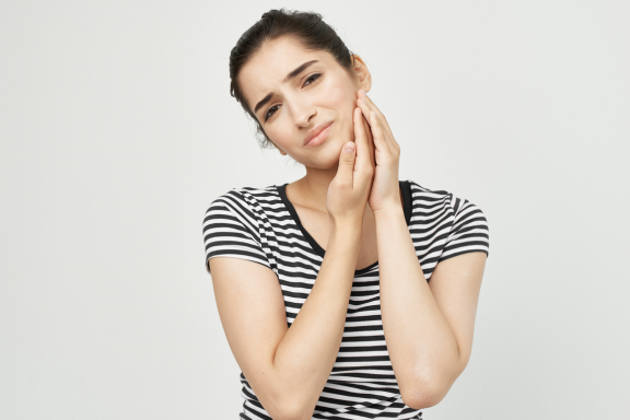teen girl holding face in pain from impacted wisdom teeth